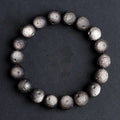 Close-up of an obsidian crater ball bead bracelet showing textured surface from grinding treatment, in silver stone meteorite finish.