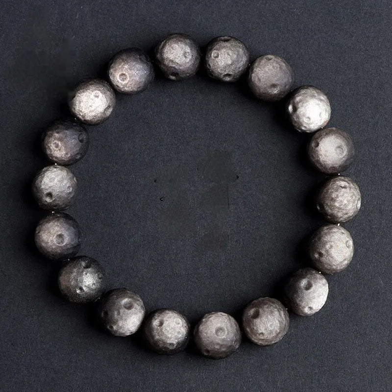 Close-up of an obsidian crater ball bead bracelet showing textured surface from grinding treatment, in silver stone meteorite finish.