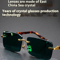 A pair of frameless sunglasses with dark green crystal lenses, shown with a soft case and cleaning cloth.