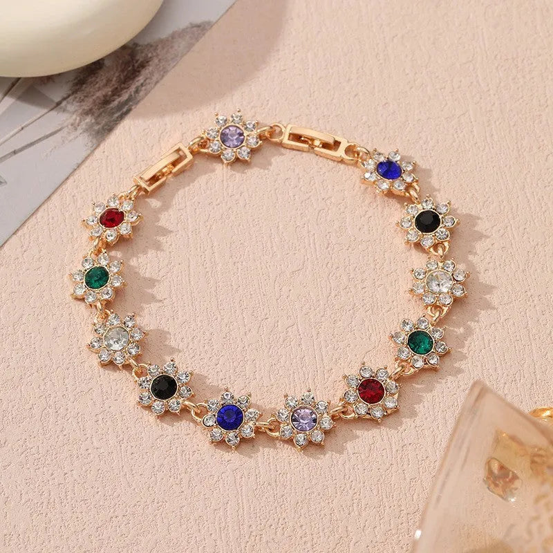 Gold tone flower-shaped bracelet with blue crystal gems on a wrist.