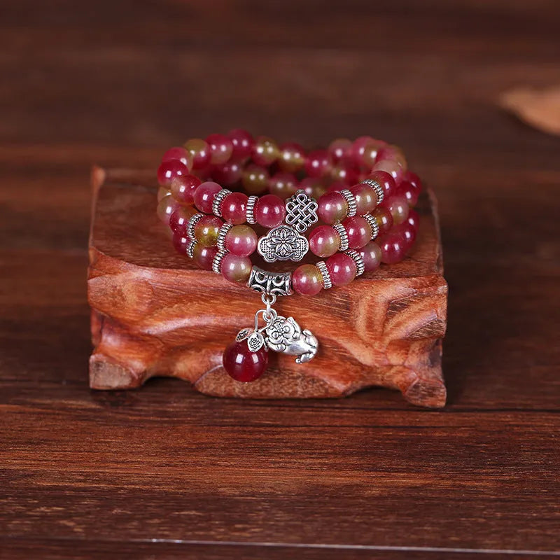 Handmade bracelet with watermelon crystal beads and a red Chinese knot on a white background.