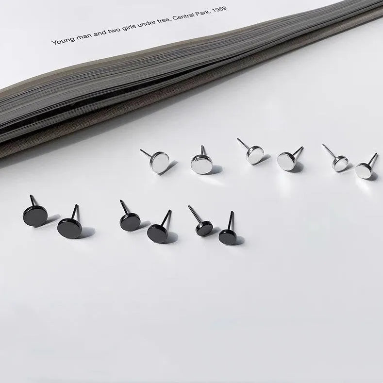 A pair of simple round sterling silver S999 stud earrings on a flat surface, shown in silver and black finishes.