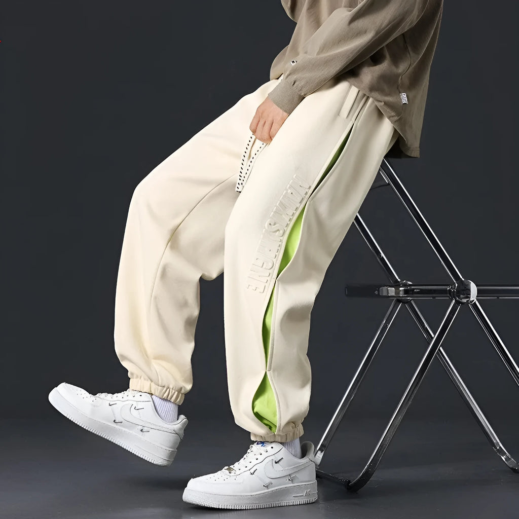 Man wearing loose grey-green cotton trousers with a banded ankle cuff and stitching detail.