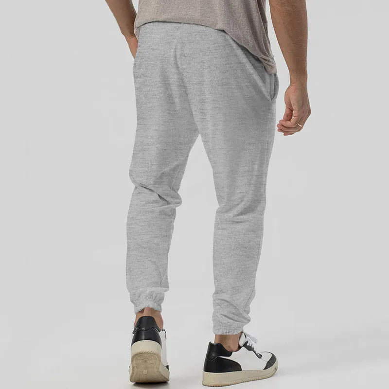 Men's grey cotton blend straight-leg track sweatpants with a mid waist and loose tapered fit on a hanger.