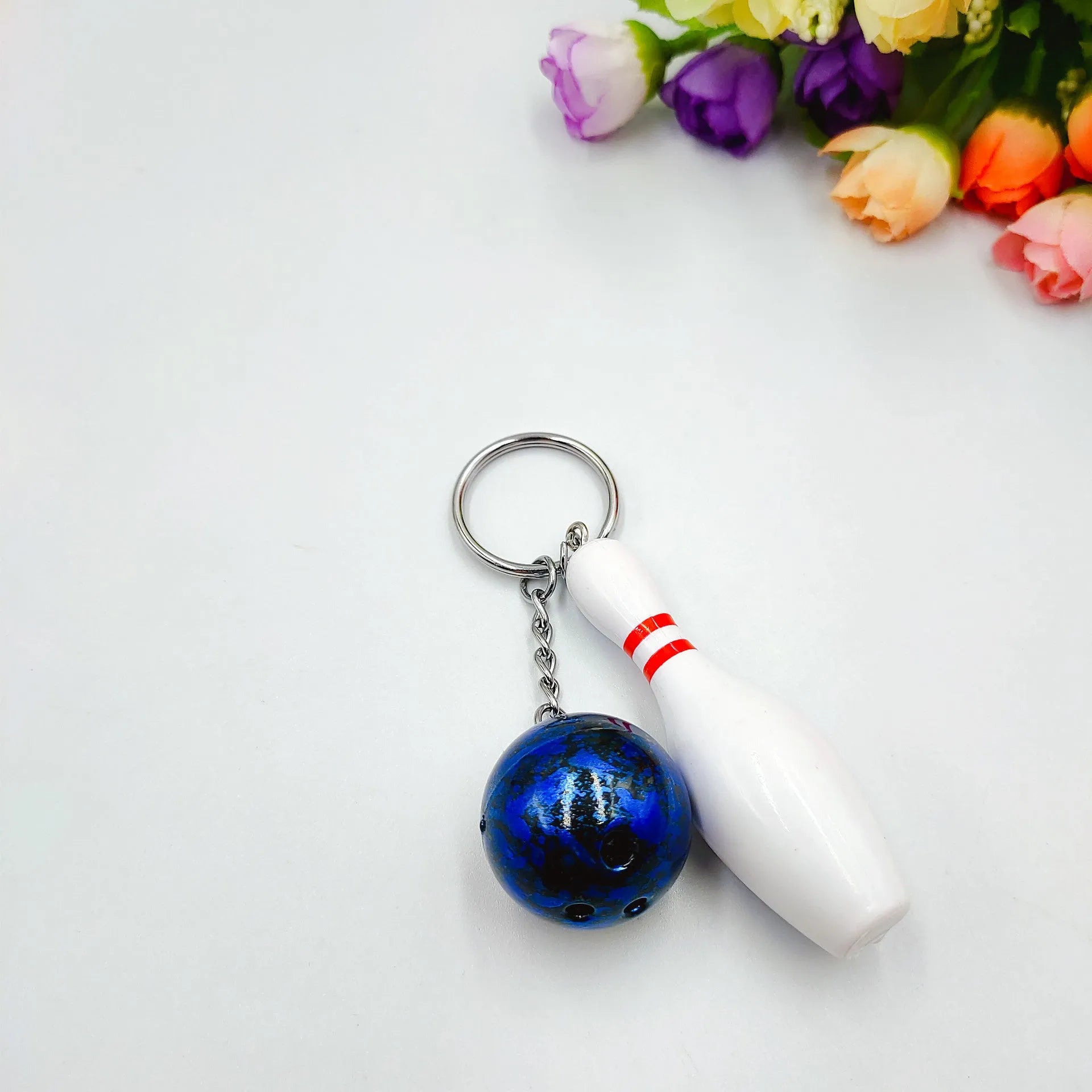Miniature blue bowling ball keychain pendant with metal keyring on a dark surface.